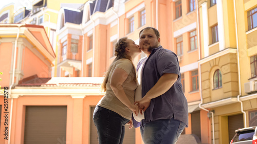 Plump woman kissing boyfriend on cheek during romantic date, taking first step