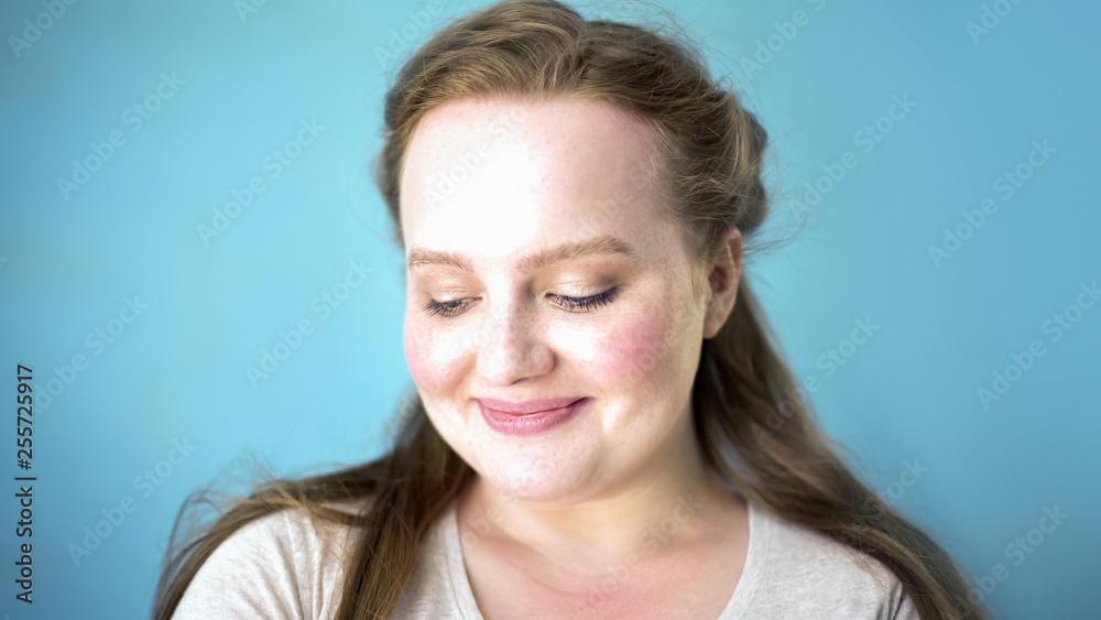 Portrait of shy plump woman with freckles, blue background, natural make up Portrait of shy plump woman with freckles, blue background, natural make up