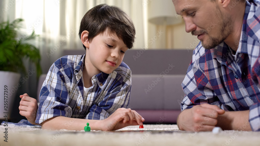 Carefree father and son playing board game, lying on floor, happy family concept Carefree father and son playing board game, lying on floor, happy family concept