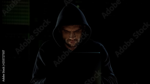 Man in hoodie typing on laptop, cyberbullying or hacking, internet security