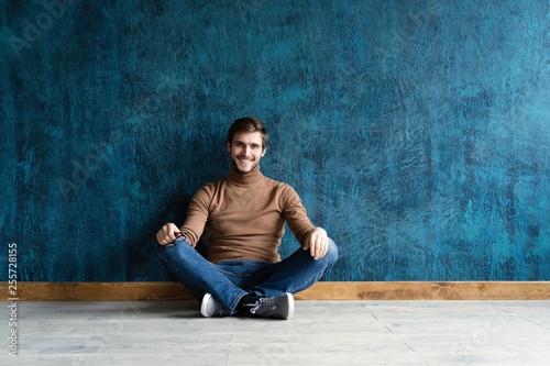 young casual fashion man sitting on the floor isolated on dark blue background.