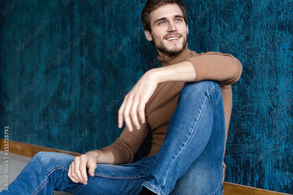 young casual fashion man sitting on the floor isolated on dark blue background. young casual fashion man sitting on the floor isolated on dark blue background.
