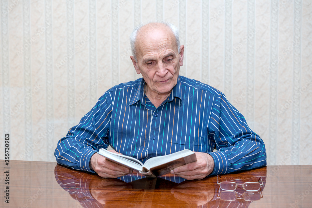 elderly man sits at a table and reads a book carefully