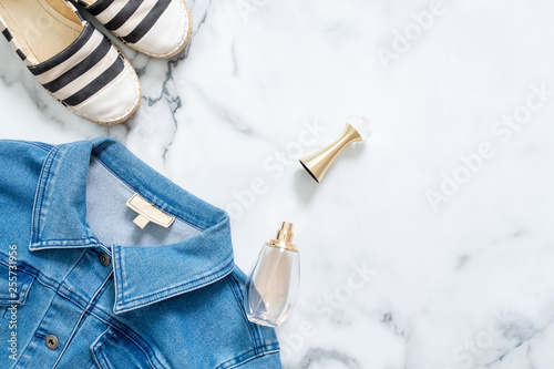 Border frame of jeans jacket, bottle of perfume, striped sandals on marble background. Flat lay design composition with feminine clothing and accessories. Beauty blogger, trendy hipster lifestyle