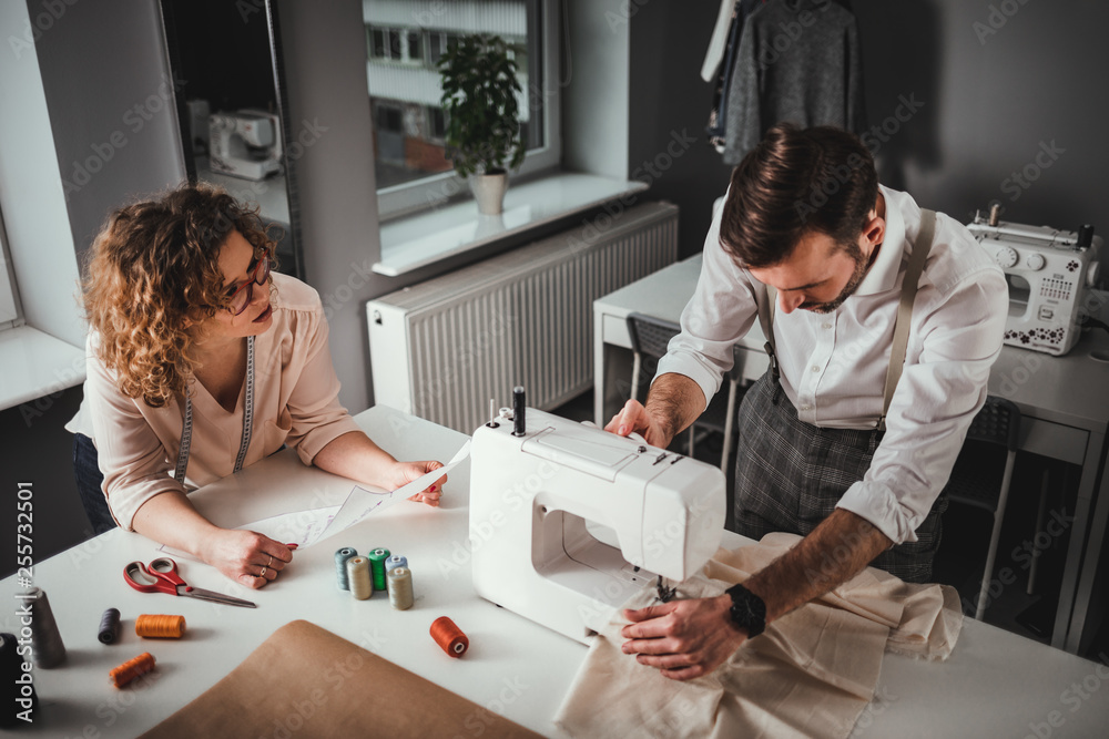 Professional tailors during work on project using sewing machine at fashion design studio