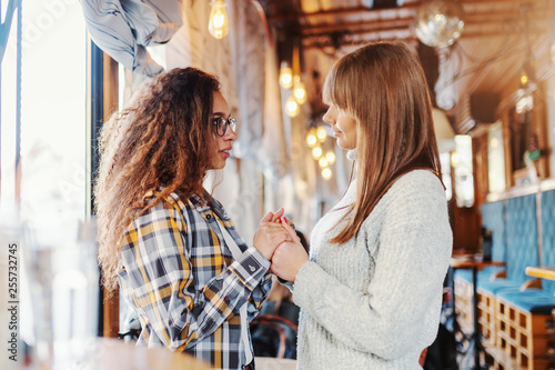 Two teenage girls holding hands and smiling while standing in cafeteria.