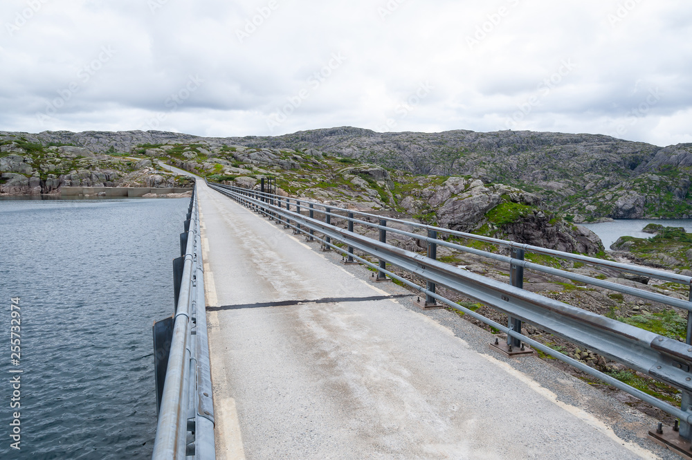 Open road on top of a small water dam. Empty road with no traffic in countryside. Rural landscape. Ryfylke scenic route. Norway. Europe.