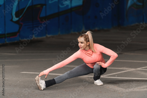 Beautiful blonde woman in sportswear stretching legs before running outdoors.