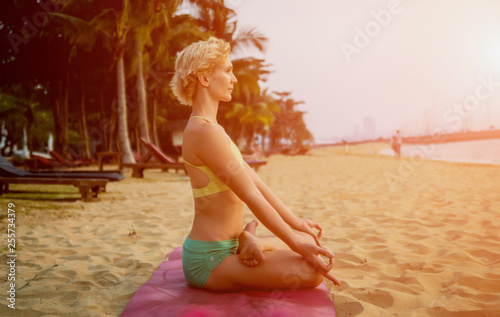 Beautiful young woman practic yoga at the beach. Early morning exercise