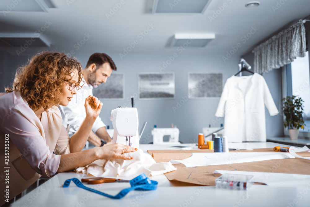 Professional tailors during work on project in fashion design studio, using sewing equipment