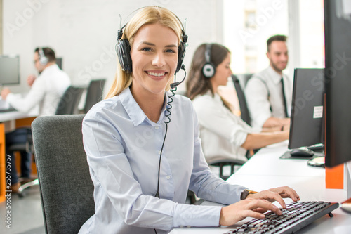 Smiling customer support worker woman with headset working on computer in call center