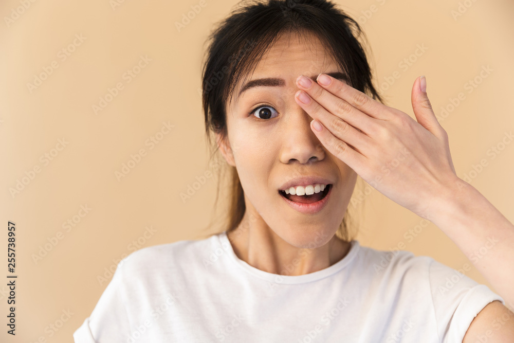 Image of attractive chinese woman wearing basic t-shirt covering her eyes and peeking Image of attractive chinese woman wearing basic t-shirt covering her eyes and peeking