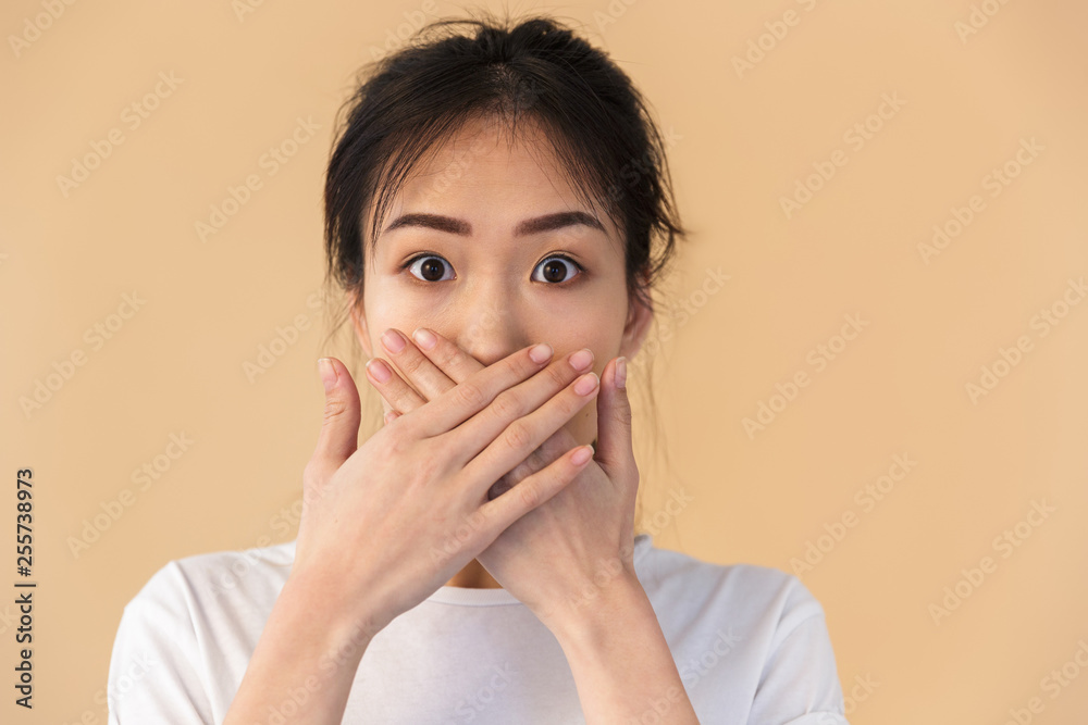 Image of silent chinese woman wearing basic t-shirt covering her mouth with hands - obrazy, fototapety, plakaty 