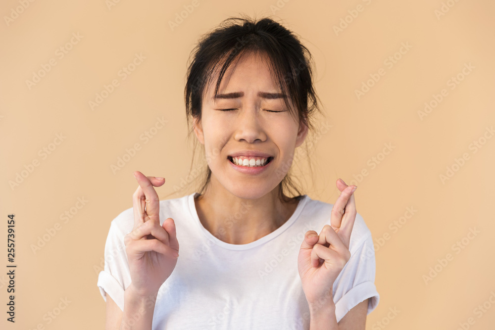 Portrait of brunette asian woman wearing basic t-shirt wishing luck with fingers crossed Portrait of brunette asian woman wearing basic t-shirt wishing luck with fingers crossed