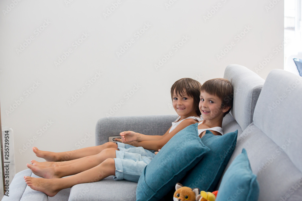 Sweet children, sitting on couch in sunny living room, playing on tablet