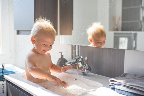 Baby Taking Bath In Sink Child Playing With Foam And Soap Bubbles In Sunny Bathroom With Window Little Boy Bathing Water Fun For Kids Hygiene And Skin Care For Children Stock Photo