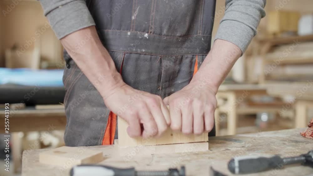 Close-up hands on unrecognizable carpenter joining two pieces of wood together. Wooden details are being joint by means of glue and dowel pins. Joiner using clamps for better glueing