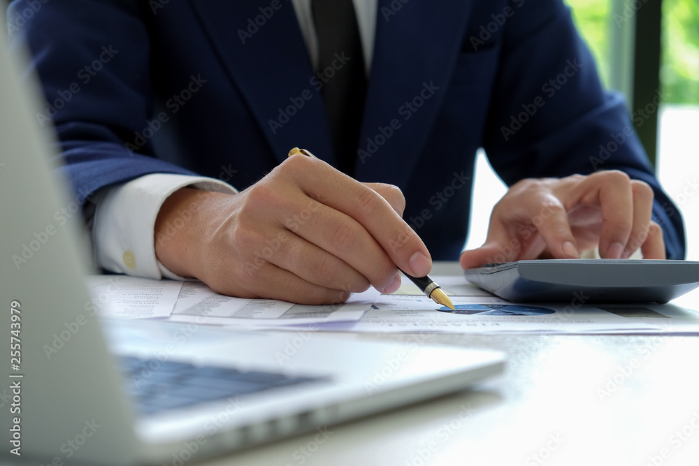 Businessman hand works on a calculator and uses a pen pointing at the graph. Businessman hand works on a calculator and uses a pen pointing at the graph.