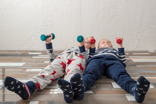 Two funny boys in sports clothes raise dumbbells up. Guys are actively engaged in fitness at home. Copy space.