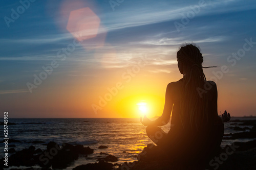 Yoga woman silhouette on the ocean during amazing sunset.