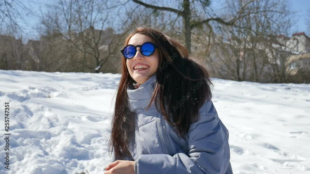 Beautiful girl in blue mirrored sunglasses and straight dark hair throwing snowballs playing with somebody outdoors in the park in the morning during sunny but cold day in early spring Beautiful girl in blue mirrored sunglasses and straight dark hair throwing snowballs playing with somebody outdoors in the park in the morning during sunny but cold day in early spring