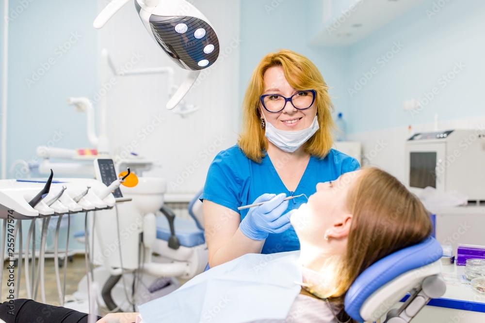 Woman dentist in blue uniform treats tools teeth girl lying on the