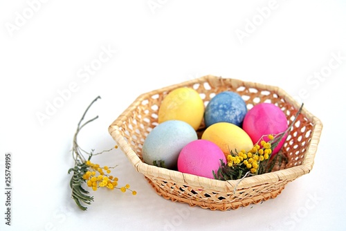Multi-colored Easter eggs in a wicker basket on a white background. Selective focus.