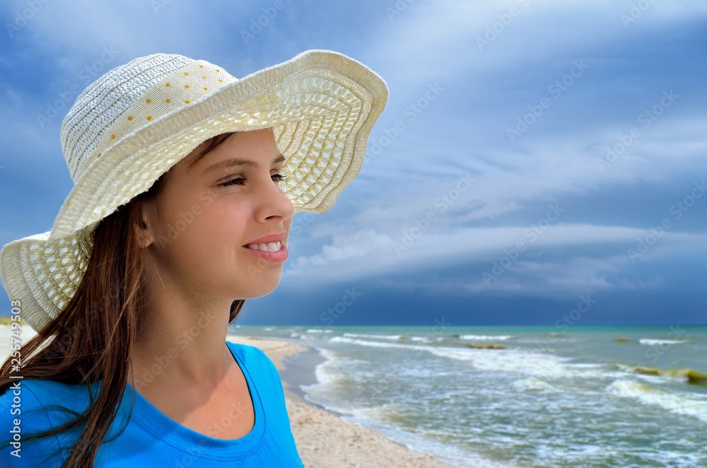 Young girl in a white hat on the sea beach. Clean, sandy beach against the blue sea.