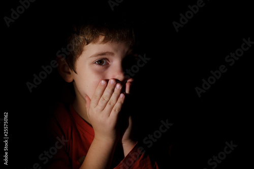 Quadro em tela Portrait in the dark of a young scared sad boy of 7 years scared and upset hands on the mouth in the dark backround in the profile