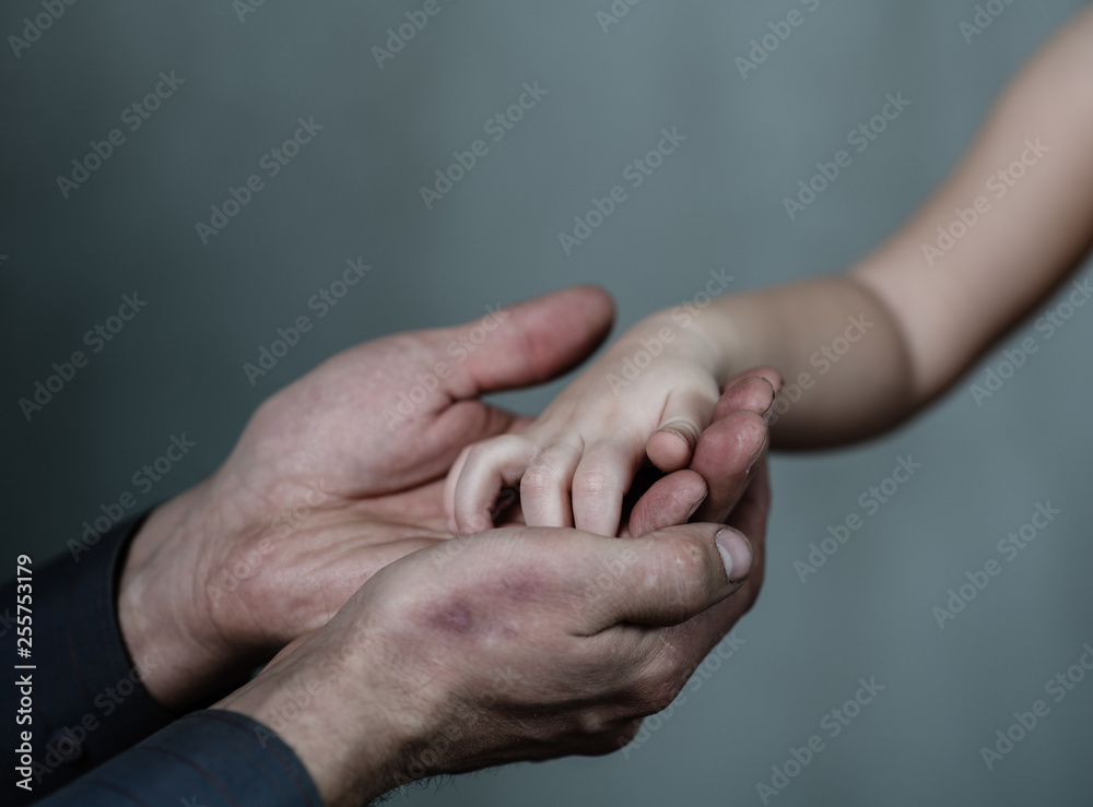 Closeup senior man and baby girl holding hands together on dark background Closeup senior man and baby girl holding hands together on dark background
