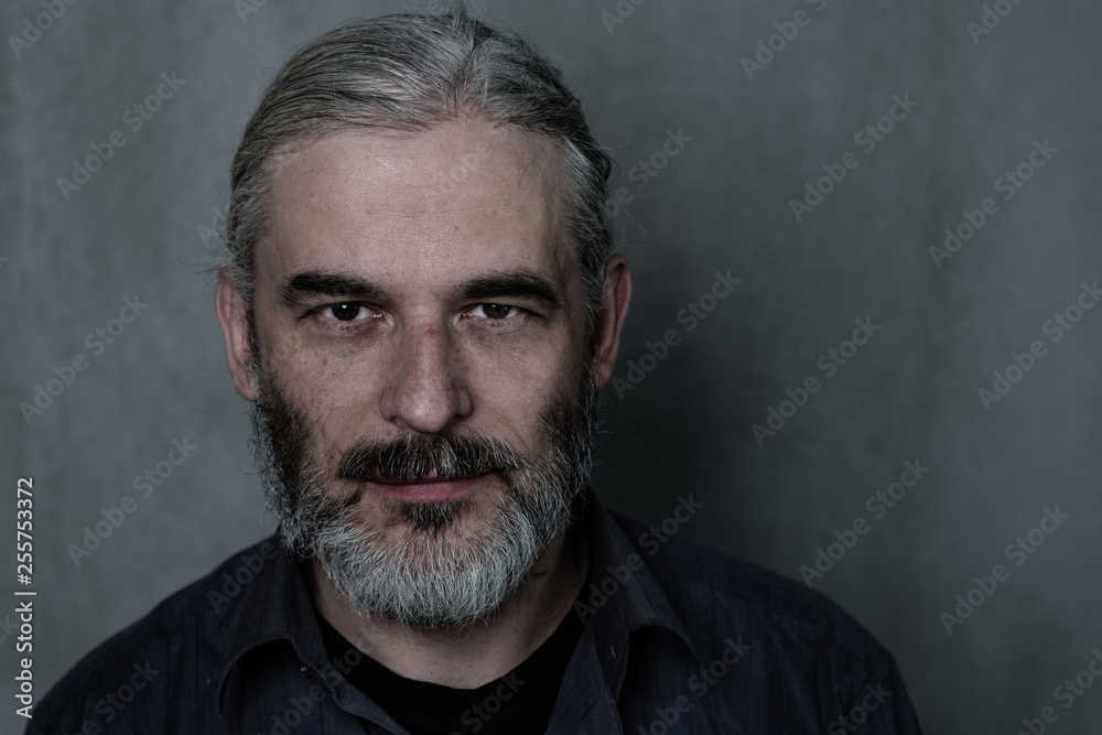 Portrait of an adult man with a gray beard and longhair on dark background. Empty space for text Portrait of an adult man with a gray beard and longhair on dark background. Empty space for text