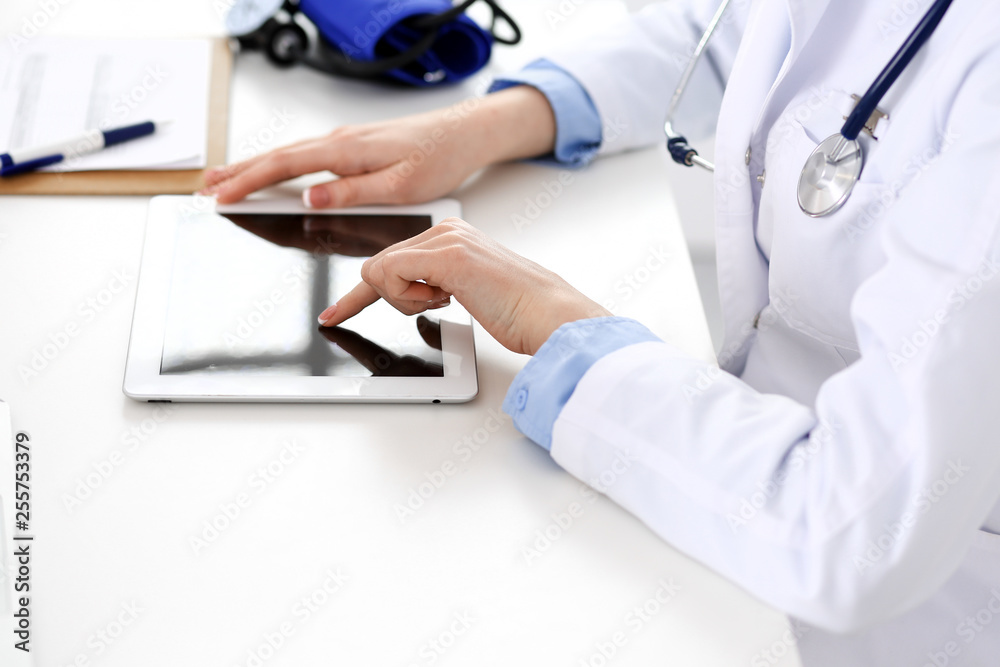 Doctor working table. Woman physician using tablet computer while sitting in hospital office close-up. Healthcare, insurance and medicine concept