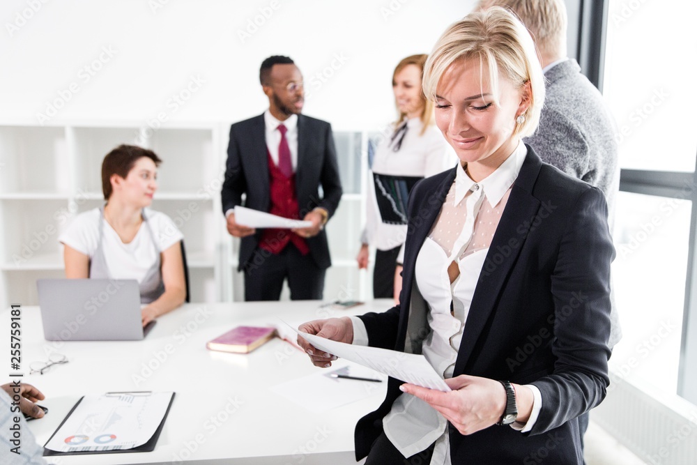 Girl office clerk stands with documents on the background of business colleagues in the office Girl office clerk stands with documents on the background of business colleagues in the office