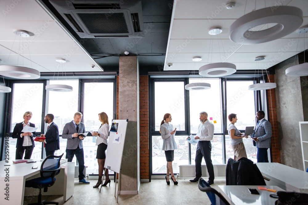Corporate business team stand with documents in one line on the background of a panoramic window in the office. Ethnic business partners Corporate business team stand with documents in one line on the background of a panoramic window in the office. Ethnic business partners
