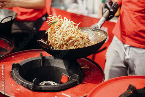 Street food chef cooking noodles and vegetables in a pan on fire at open kitchen. Fried noodles in a wok on the open fire. Asian street food festival in city photo