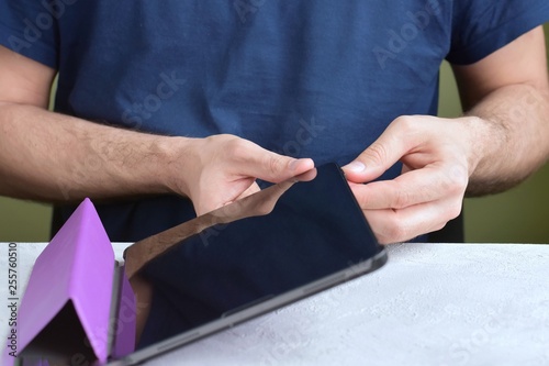 Blurred caucasian man puts on a new purple leather case on tablet with selective focus. White male hands are holding a tablet and putting on a violet cover. Man using a digital tablet