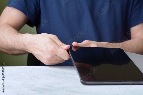 Blurred caucasian man puts on a new purple leather case on tablet with selective focus. White male hands are holding a tablet and putting on a violet cover. New case for digital gadget
