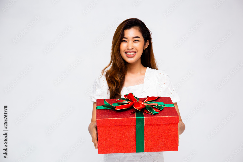 Lovely Asian female smiling and giving big gift box to camera while standing on gray background Lovely Asian female smiling and giving big gift box to camera while standing on gray background