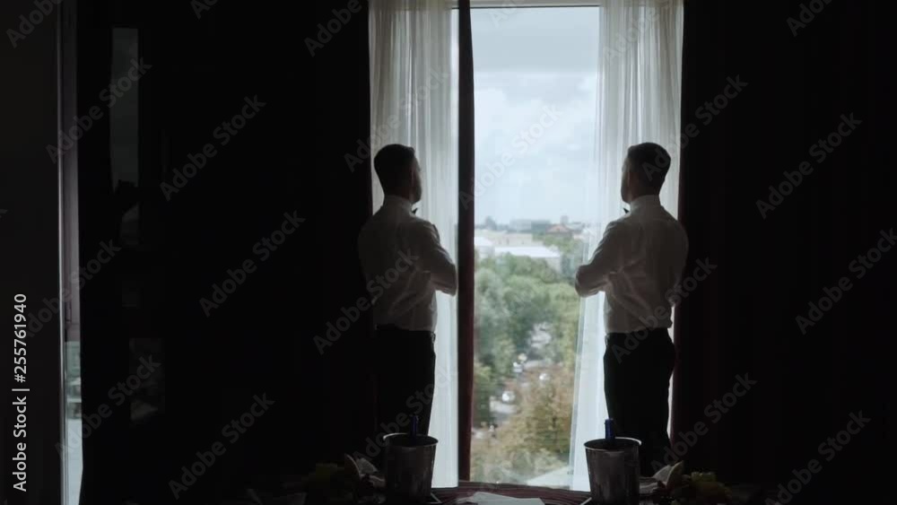 Elegant successful man stands near the panoramic window of luxury apartments and buttons shirt. luxury concept Elegant successful man stands near the panoramic window of luxury apartments and buttons shirt. luxury concept
