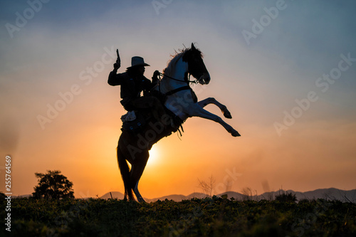 silhouette cowboy fire a gun on a horse back in sunset