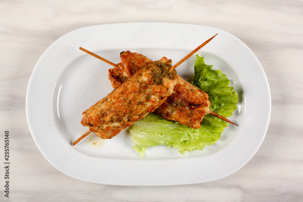 Meat kebab on wooden skewers with a leaf of green lettuce.