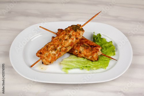 Meat kebab on wooden skewers with a leaf of green lettuce.