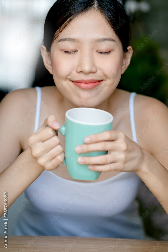 beautiful asian teen white Tank top happiness smile enjoy freshness morning with hot drink near window with sun light beautiful asian teen white Tank top happiness smile enjoy freshness morning with hot drink near window with sun light