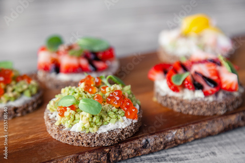 Сloseup macro set of different northern trendy appetizers on smorrebrod rye bread with red caviar and avocado, strawberries, balsamic dressing. Concept quick snack in wine bar, food shooting