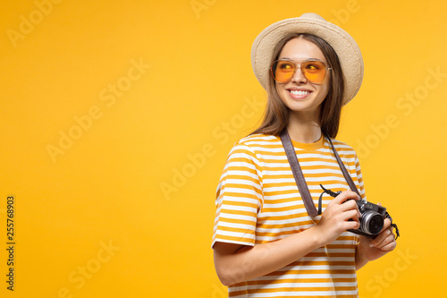 Tourism concept. Horizontal banner of excited young female tourist holding photo camera, isolated on yellow background with copy space