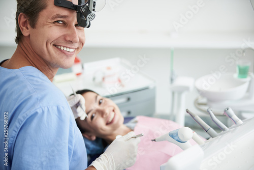 Cheerful male dentist with instruments standing near patient