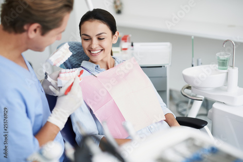 Male dentist showing teeth model to smiling young lady