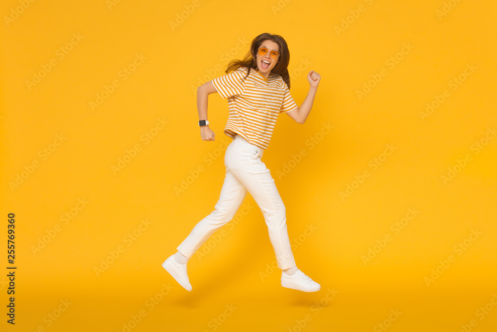 Happy funny sporty girl jumping like she walking in the air, isolated on yellow background