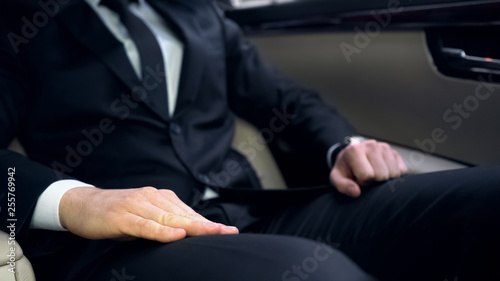 Nervous man in suit sitting on backseat of car, late for important meeting