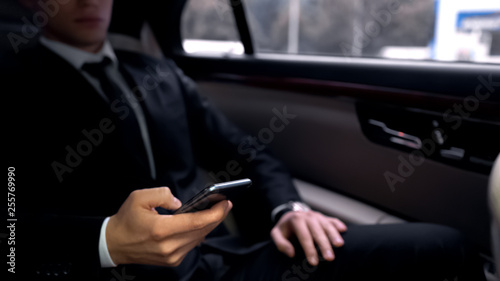 Successful businessman in luxury auto, scrolling smartphone, reading e-mail app © motortion